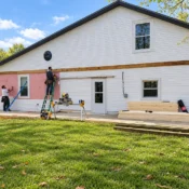 Contractors installing exterior siding on a white residential home during a renovation project.
