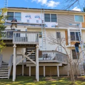 Contractors installing new exterior siding on a multi-story home using ladders and scaffolding.