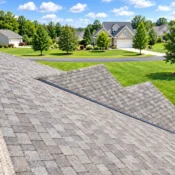Close-up view of a gray asphalt shingle roof overlooking a well-maintained suburban neighborhood on a sunny day.