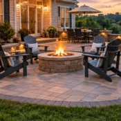 Paver patio with a stone fire pit, Adirondack chairs, lit seating walls and an outdoor dining area at sunset.