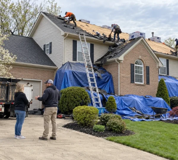 Roofers in safety harnesses installing underlayment and metal flashing beside a brick chimney during a roof replacement.