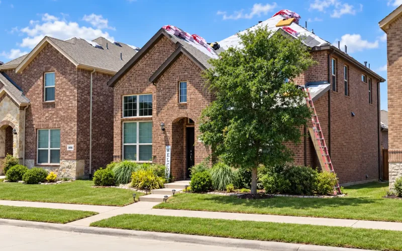 Brick home undergoing a roof replacement with roofing underlayment, new shingles, and a ladder positioned along the side.