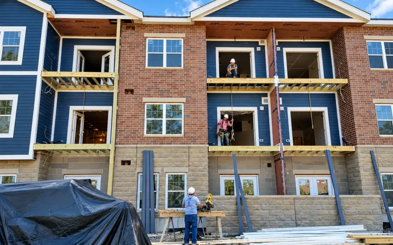 Construction crew working on the exterior of a multi-story residential building with brick and blue siding.