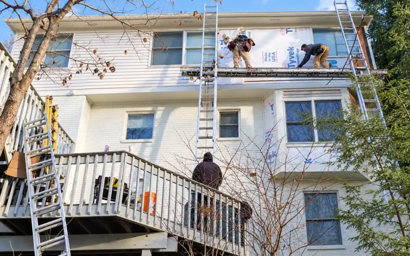 Construction crew installing exterior siding and house wrap on the upper level of a residential home.